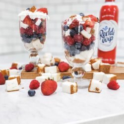 Countertop with parfait cups filled with angel food cake, blueberries, strawberries, and raspberries with Reddi Whip can behind