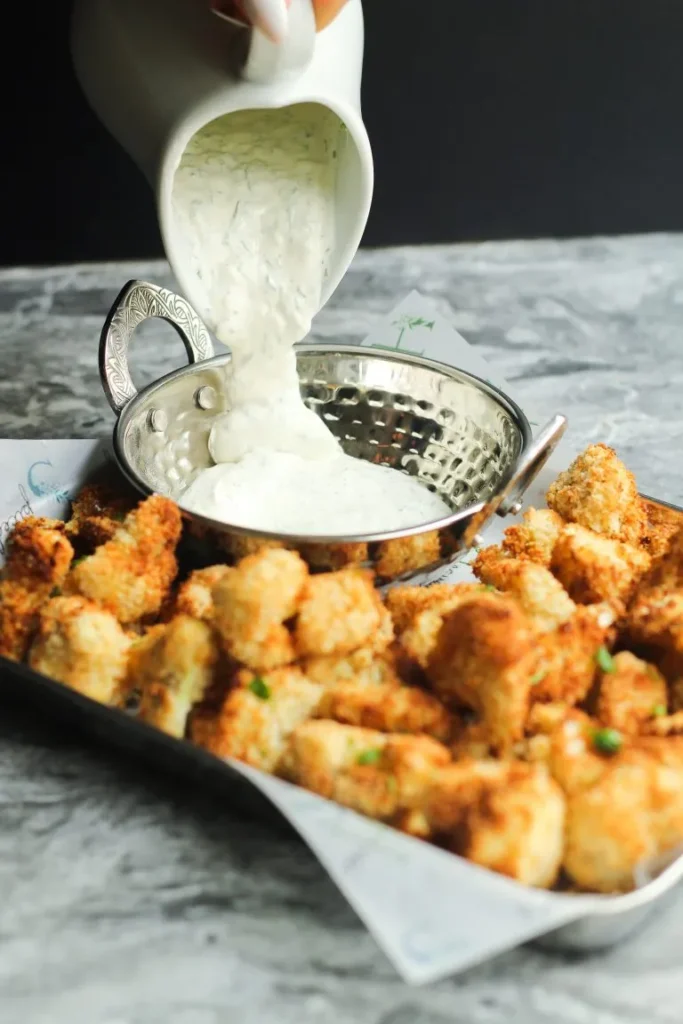 Crispy cauliflower bites served in a white bowl with dipping sauce on the side, a healthy New Year’s Eve snack idea