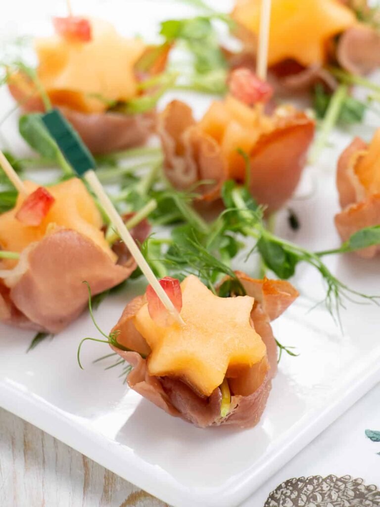 Crispy ham and melon appetizers on a decorative platter, a sweet and savory New Year’s Eve snack idea.