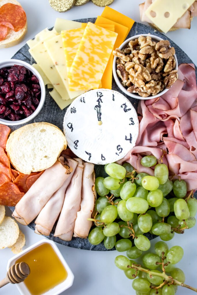 Festive New Year’s charcuterie board arranged with meats, cheeses, and fruits in a clock design to countdown to midnight.