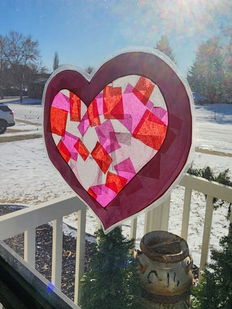 A vibrant sun catcher heart made from tissue paper, hanging on a glass door