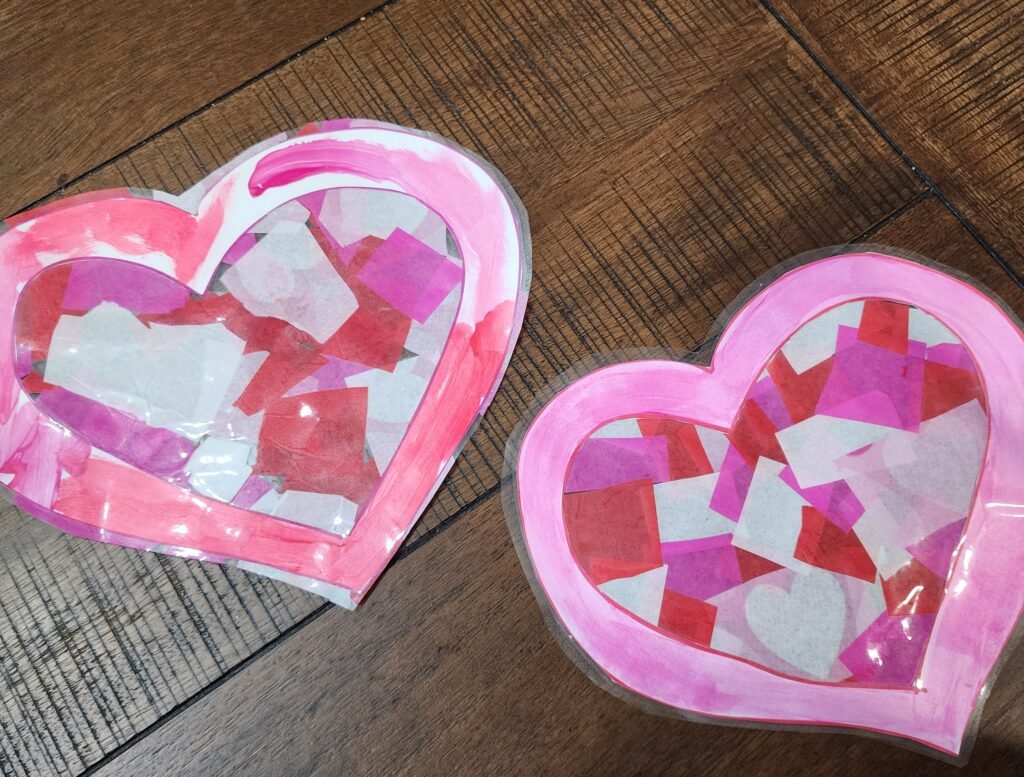 Craft for kids: A parent and child pressing a second sheet of contact paper over a heart sun catcher to seal it