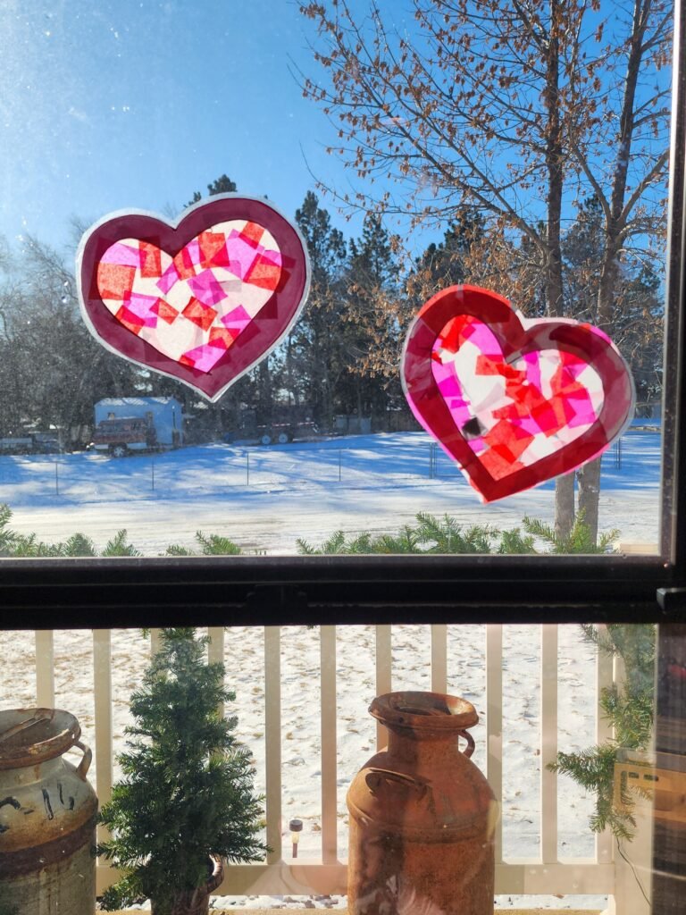 Valentine’s Day arts and crafts: A finished sun catcher heart taped to a window, glowing in natural light