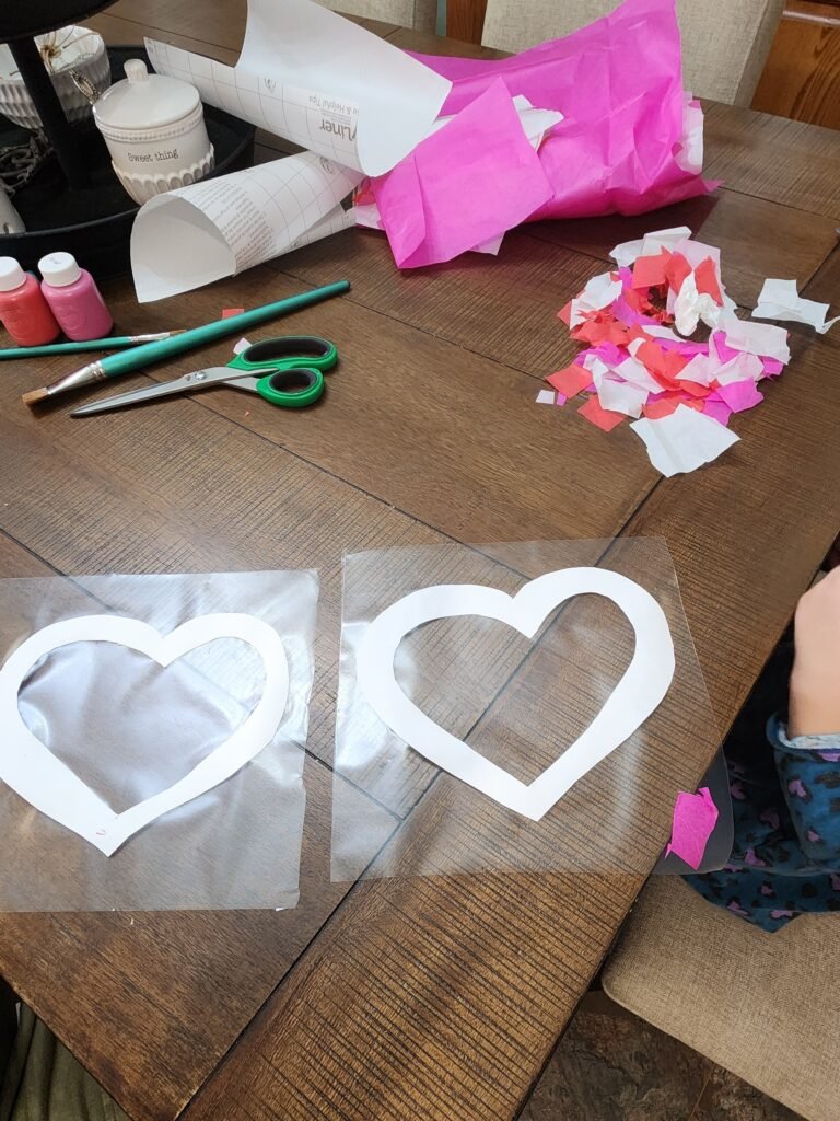 Valentine’s Day crafts for kids: Little hands placing tissue paper pieces inside a heart outline on sticky contact paper