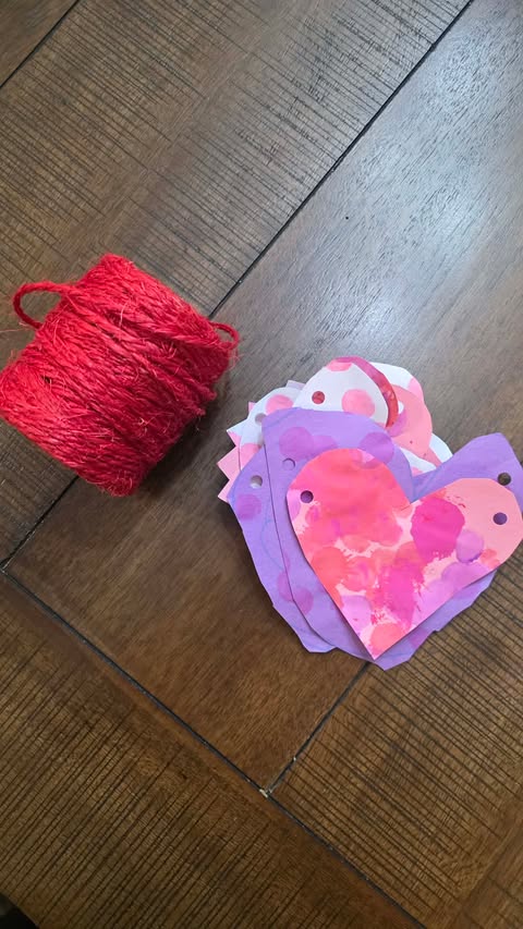 Threading twine through the holes we punched on the craft paper hearts to string them into a banner